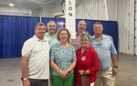 Six adults stand together indoors beside a sign reading "Dillon," smiling for a group photo at what appears to be an event or convention.