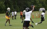 A football player in white catches a pass during a game, with teammates and opponents in green and yellow uniforms on the field.