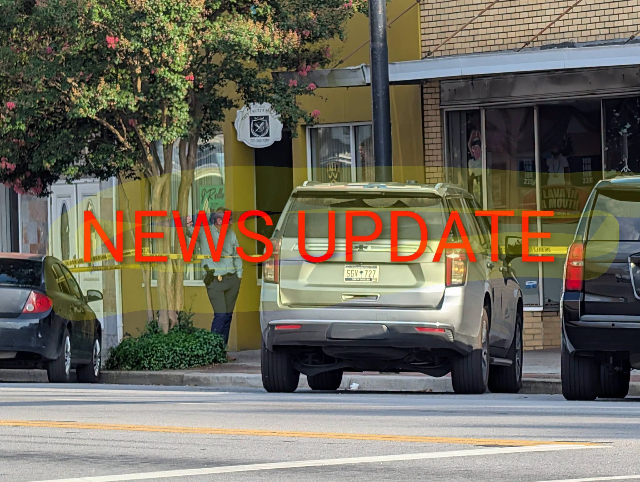 Police officer stands near vehicles and yellow caution tape outside a building, with large "NEWS UPDATE" text overlayed on the image.