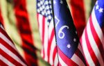 Close-up of several American flags, including a Betsy Ross flag with "76" in white, symbolizing the year 1776, with blurred flags in the background.