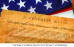 The Declaration of Independence document with a partial view of the American flag in the background.