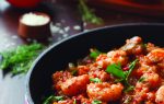 A close-up of shrimp jambalaya in a black skillet, garnished with fresh herbs, with bell peppers and rice in the background.
