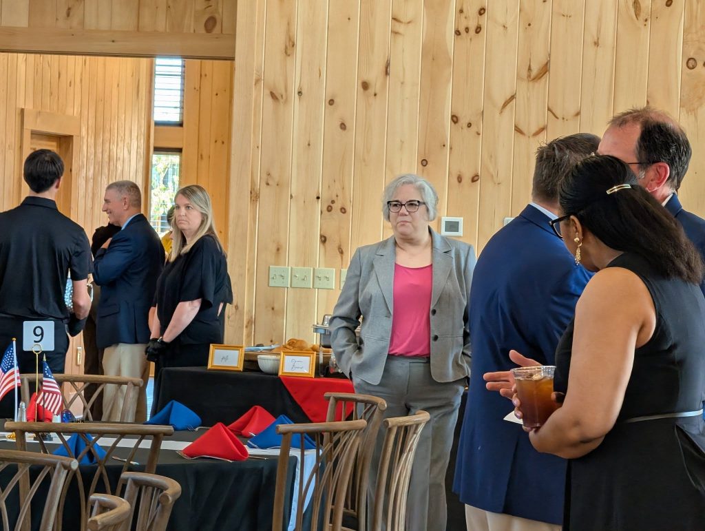 People socializing at an indoor event with wooden walls, decorated tables with red and blue napkins, and small American flags on display.