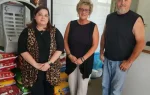 Three adults stand in a veterinary clinic next to pet supplies, with a sign reading "Dr. Kenneth L. Huggins, DVM Building" on the wall behind them.