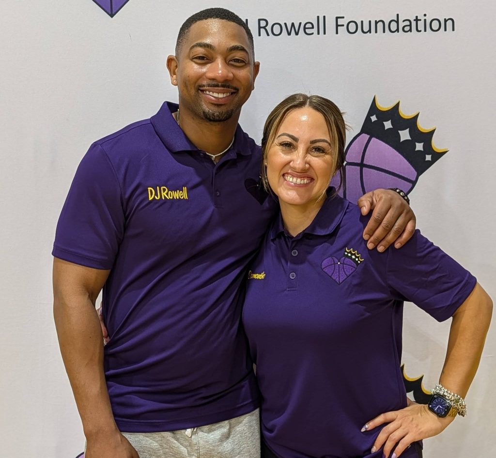Two people smiling and posing together, both wearing matching purple polo shirts with embroidered names and basketball crown logos, standing in front of a “Rowell Foundation” backdrop.