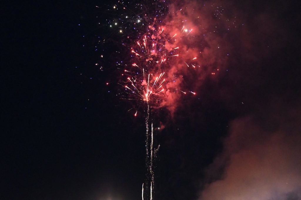 Bright red and white fireworks exploding in the night sky, with smoke and sparkling lights spreading outward.