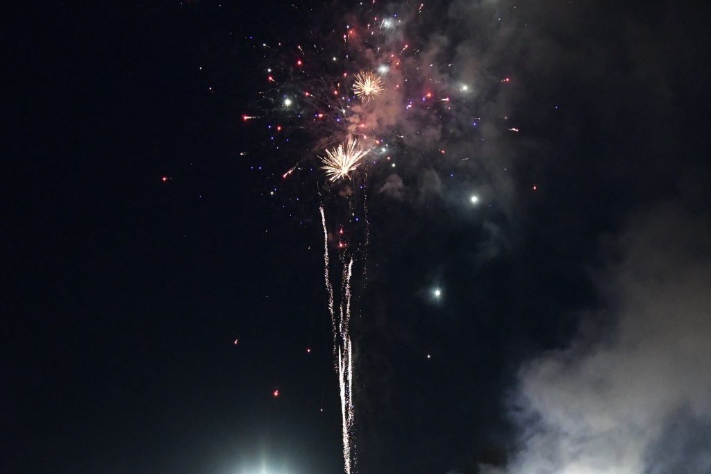 Bright fireworks exploding in the night sky, surrounded by smoke and scattered sparks, illuminating the darkness with colorful lights.