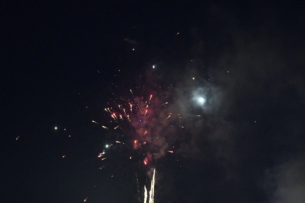 Fireworks exploding in the night sky, with bright sparks and colorful bursts surrounded by smoke and a glowing moon.