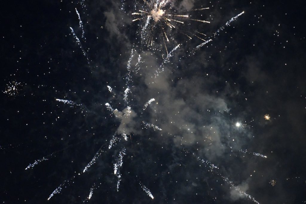 Bright fireworks explode in the night sky, creating patterns of light and smoke against a dark background.