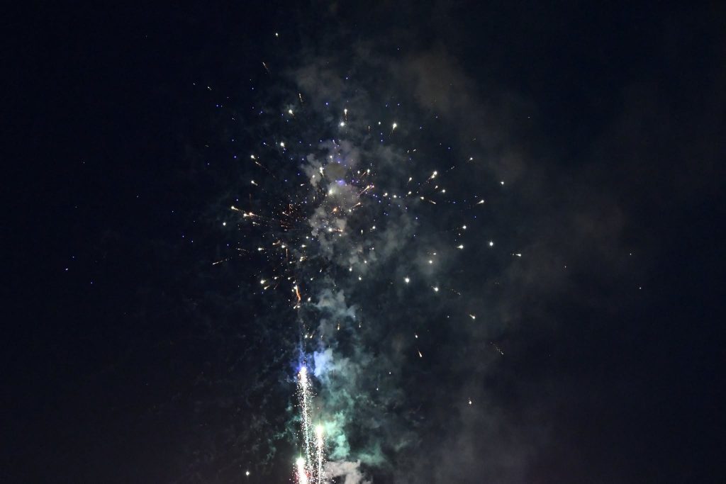 Colorful fireworks bursting in the night sky, with smoke and sparkling lights spreading across the dark background.