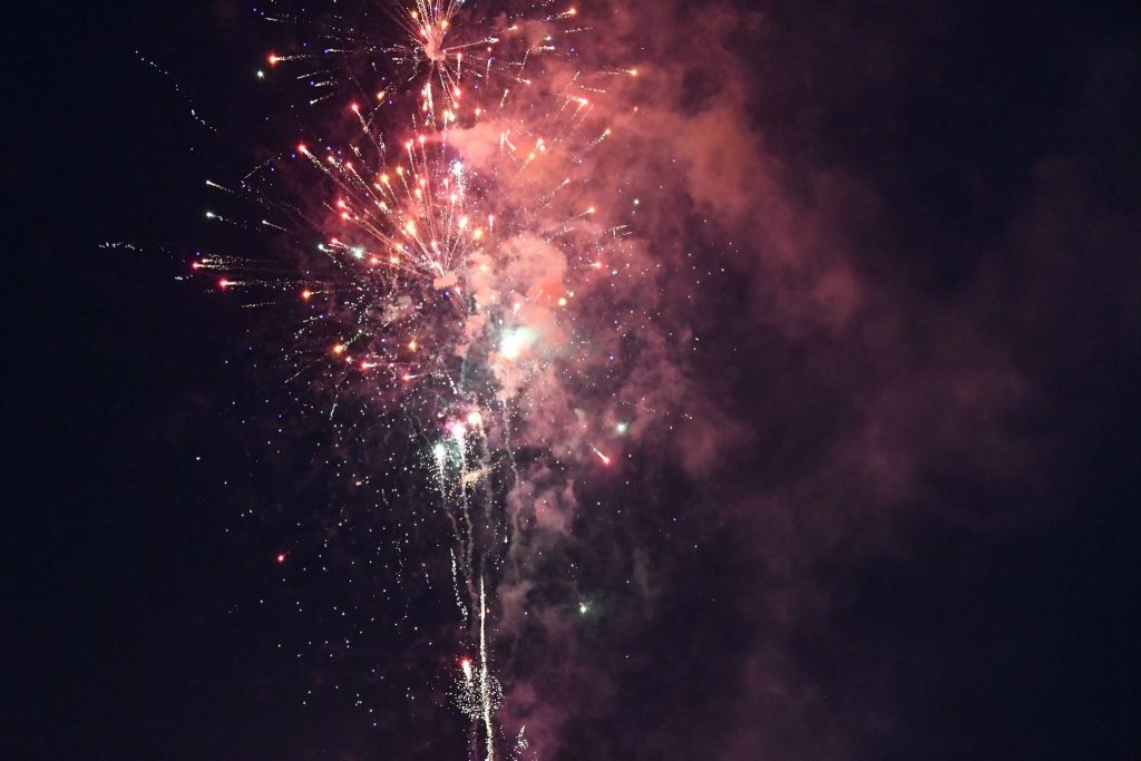 Colorful fireworks explode in the night sky, creating bright bursts of light and smoke against a dark background.