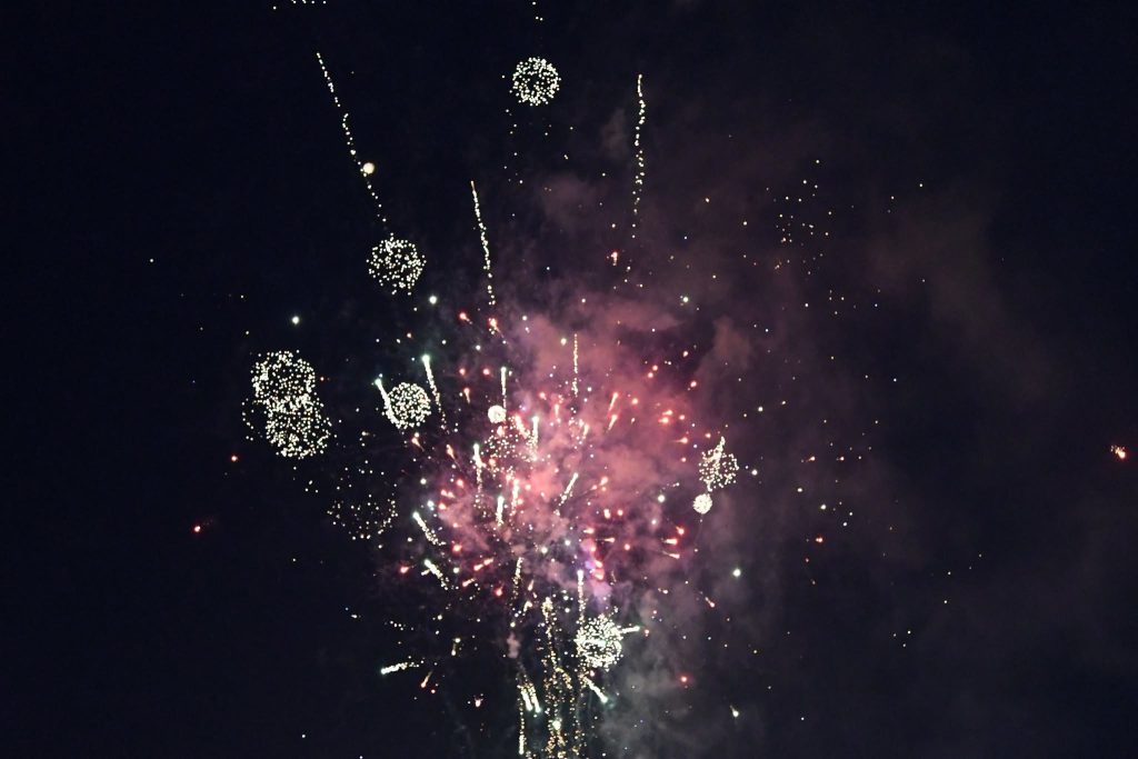 Colorful fireworks explode against a dark night sky, with bright sparks and smoke creating a festive atmosphere.