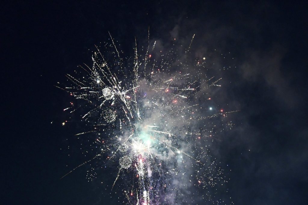 Bright fireworks exploding in the night sky, with sparkling lights and smoke creating a festive atmosphere.