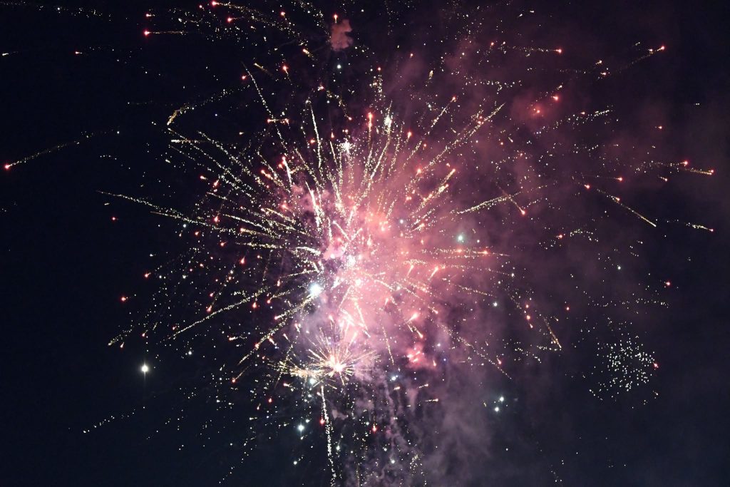 Bright fireworks burst in the night sky, with colorful sparks and smoke spreading in all directions against a dark background.