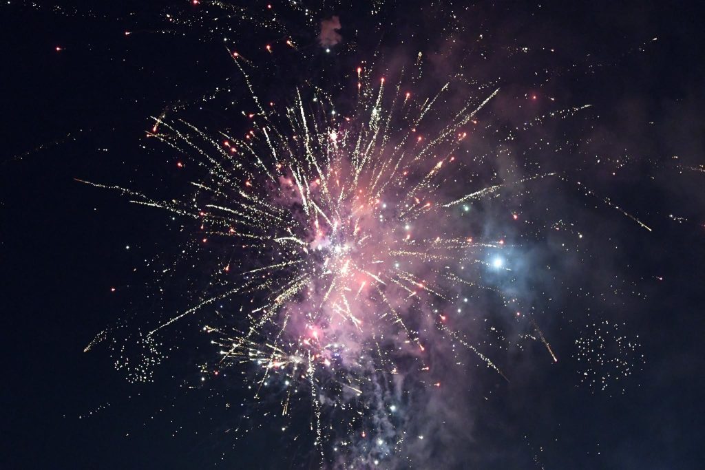 Colorful fireworks burst in the night sky, with sparkling trails and smoke creating a vibrant celebration atmosphere.
