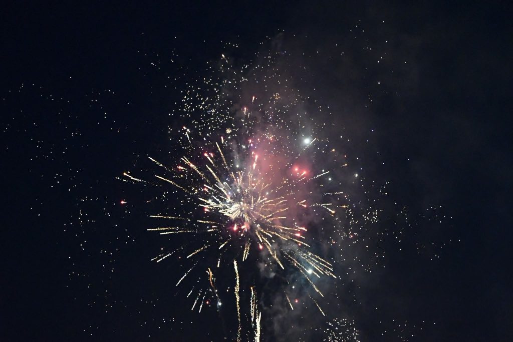 Colorful fireworks bursting in the night sky, with sparkling lights and smoke spreading out in different directions against a dark background.