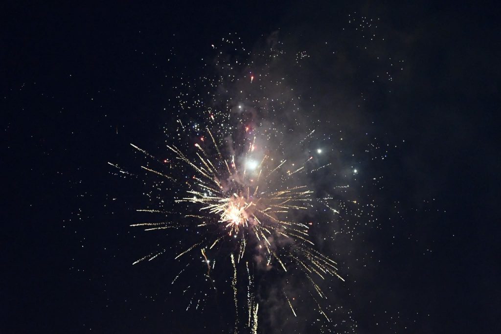 Colorful fireworks burst in the night sky, creating bright streaks and sparkling particles against a dark background.