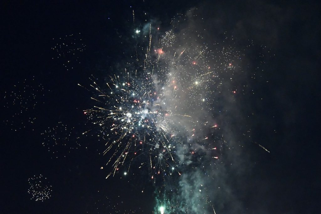 Colorful fireworks exploding in the night sky, with bright sparks and smoke spreading outward against a dark background.