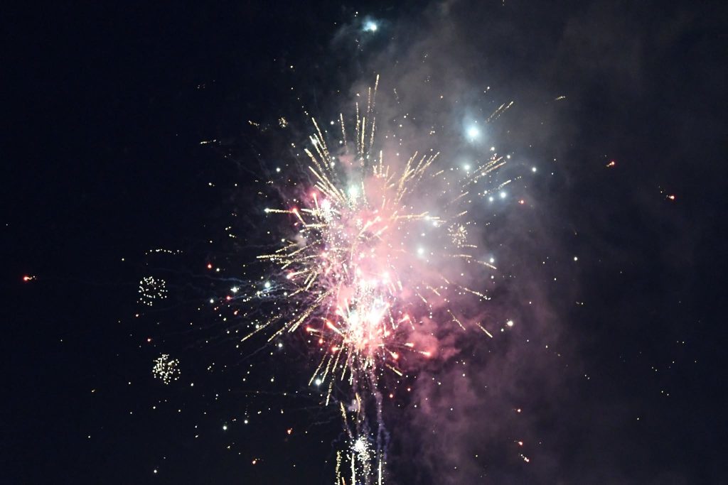 Bright fireworks exploding in the night sky, with colorful sparks and smoke spreading outwards against a dark background.