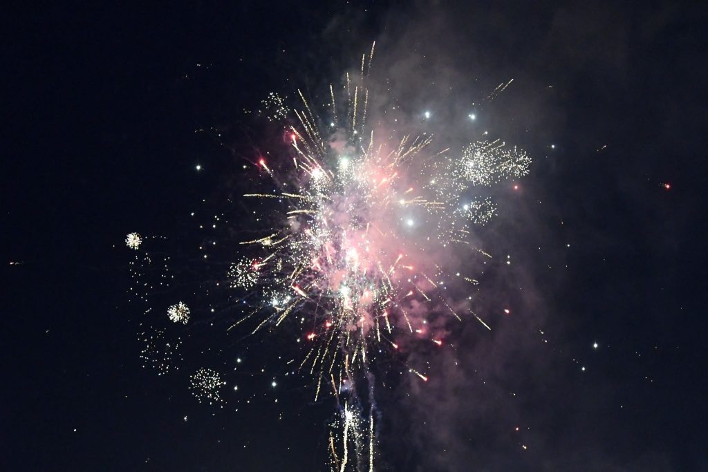 Bright fireworks explode in the night sky, emitting colorful sparks and smoke, creating a festive and celebratory atmosphere against a dark background.