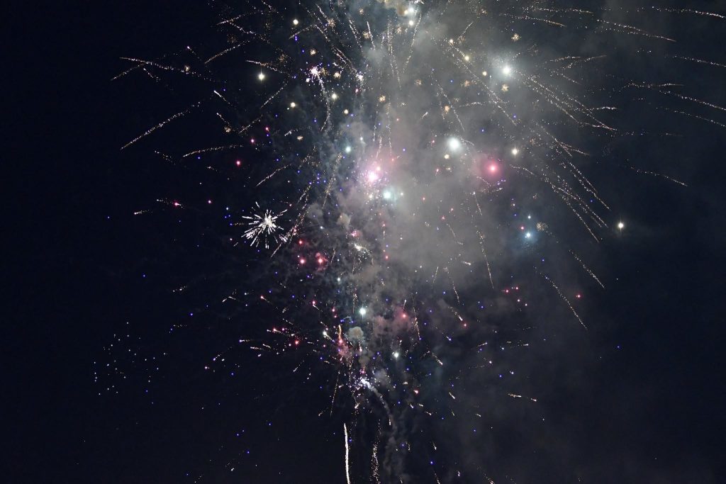 Colorful fireworks exploding in the night sky, surrounded by smoke, light trails, and sparkling bursts of red, blue, and white.
