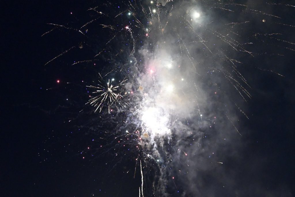 Bright fireworks exploding in the night sky, emitting colorful sparks and smoke, against a dark background.