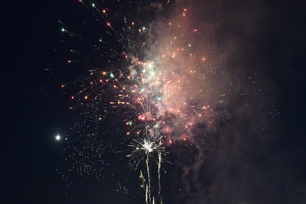 Colorful fireworks exploding in the night sky with smoke and a bright star or planet visible on the left side.