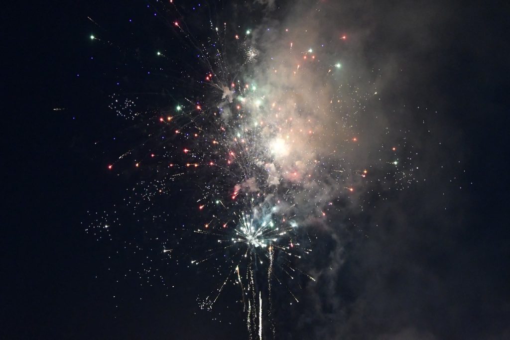 Bright fireworks bursting in the night sky, creating colorful sparks and smoky patterns against a dark background.