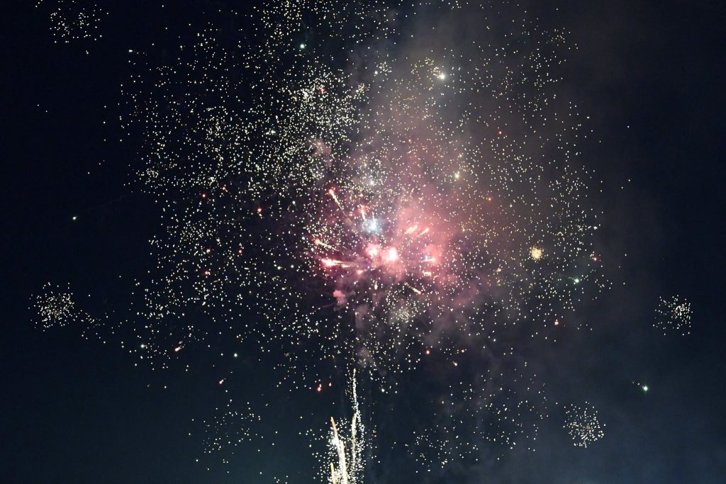 Bright fireworks explode in the night sky, creating a burst of colorful lights and sparkling effects surrounded by smoke.