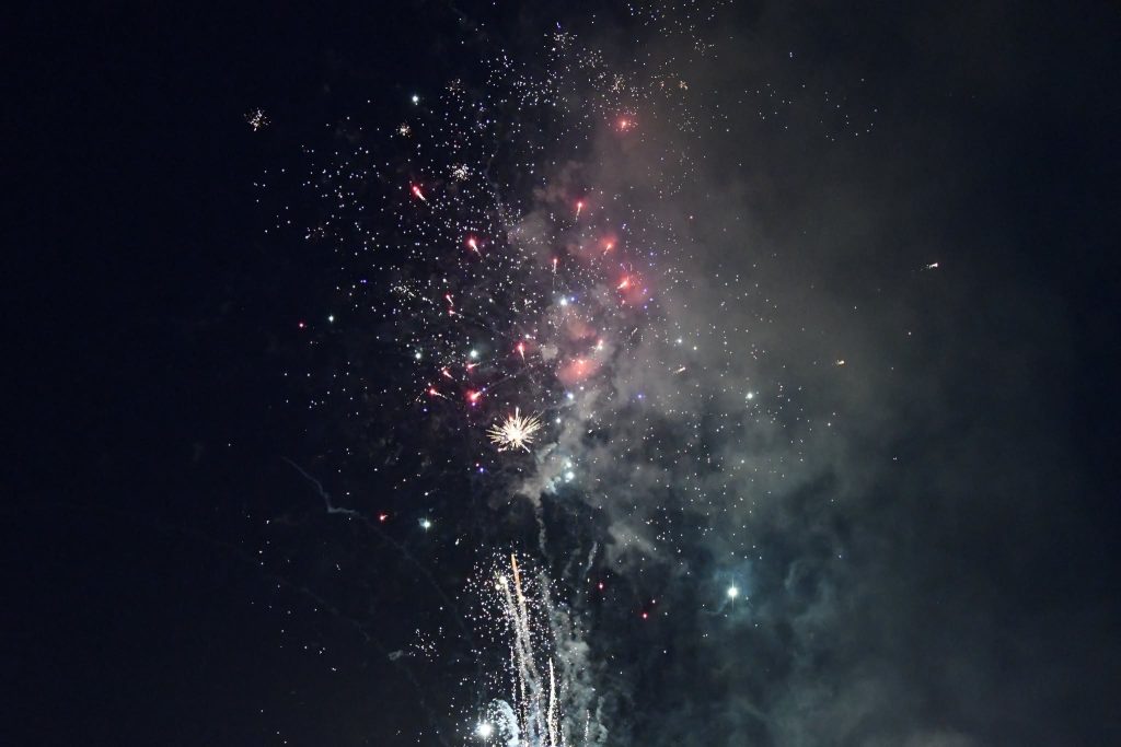 Colorful fireworks exploding in the night sky, surrounded by smoke and sparkling lights.