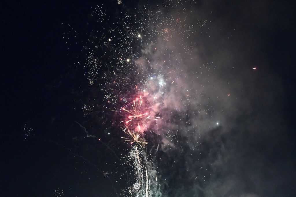 Colorful fireworks explode in the night sky, creating bright sparks and smoke against the dark background.