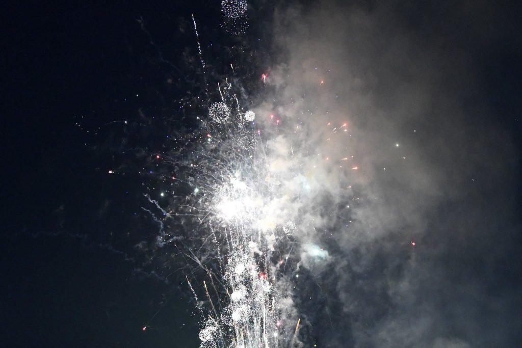 Bright fireworks exploding in the night sky, creating sparkling bursts and smoke against a dark background.