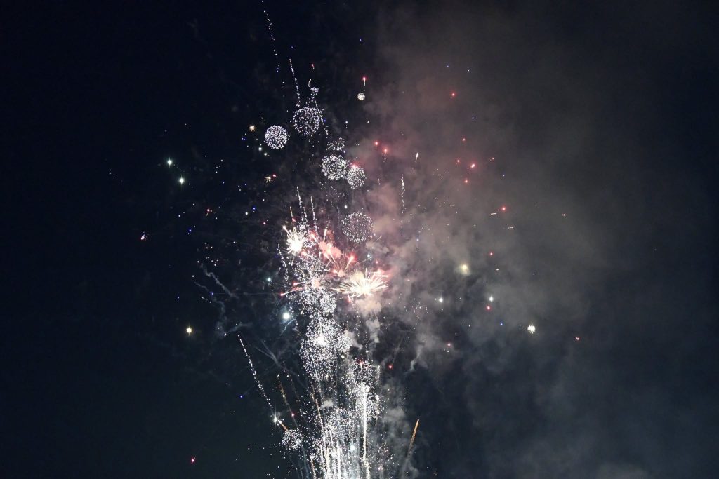 Colorful fireworks explode against a dark night sky, creating bright sparks and smoke in various shapes and patterns.