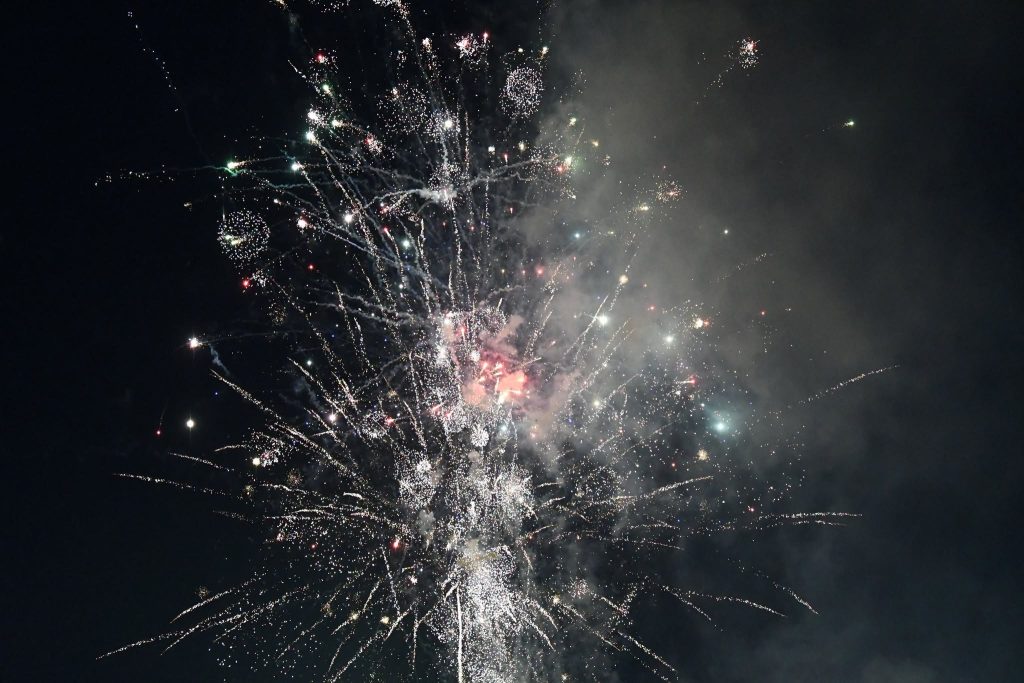 Bright fireworks explode in the night sky, creating sparkling trails and clouds of smoke.