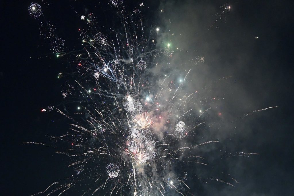 Colorful fireworks burst and sparkle against a dark night sky, creating bright, glowing trails and clouds of smoke.