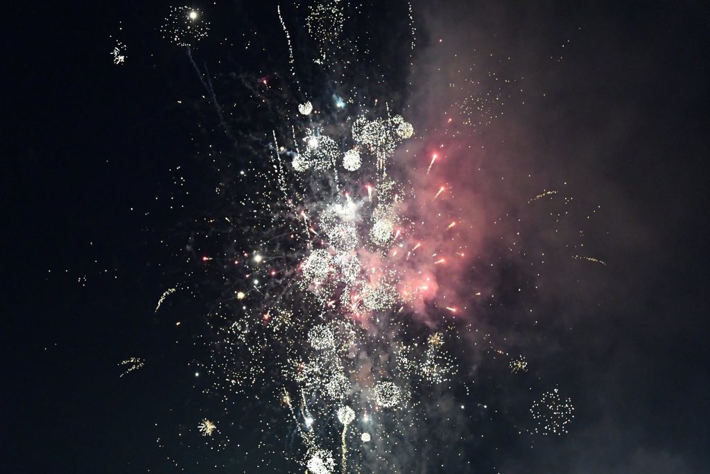 Bright fireworks exploding in the night sky, with clusters of sparkling lights and a cloud of colored smoke.