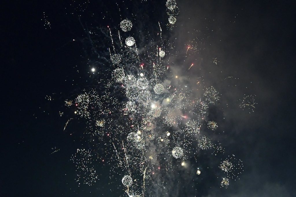 Bright fireworks burst in the night sky, creating sparkling patterns with trails of smoke and glittering lights against a dark background.