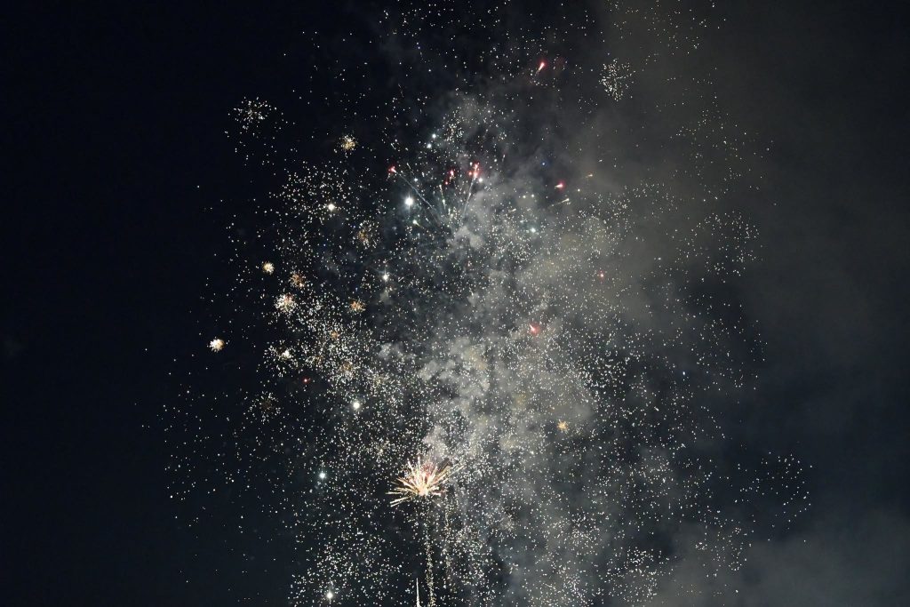 Bright fireworks exploding in the night sky, scattering sparkling lights and smoke against a dark background.