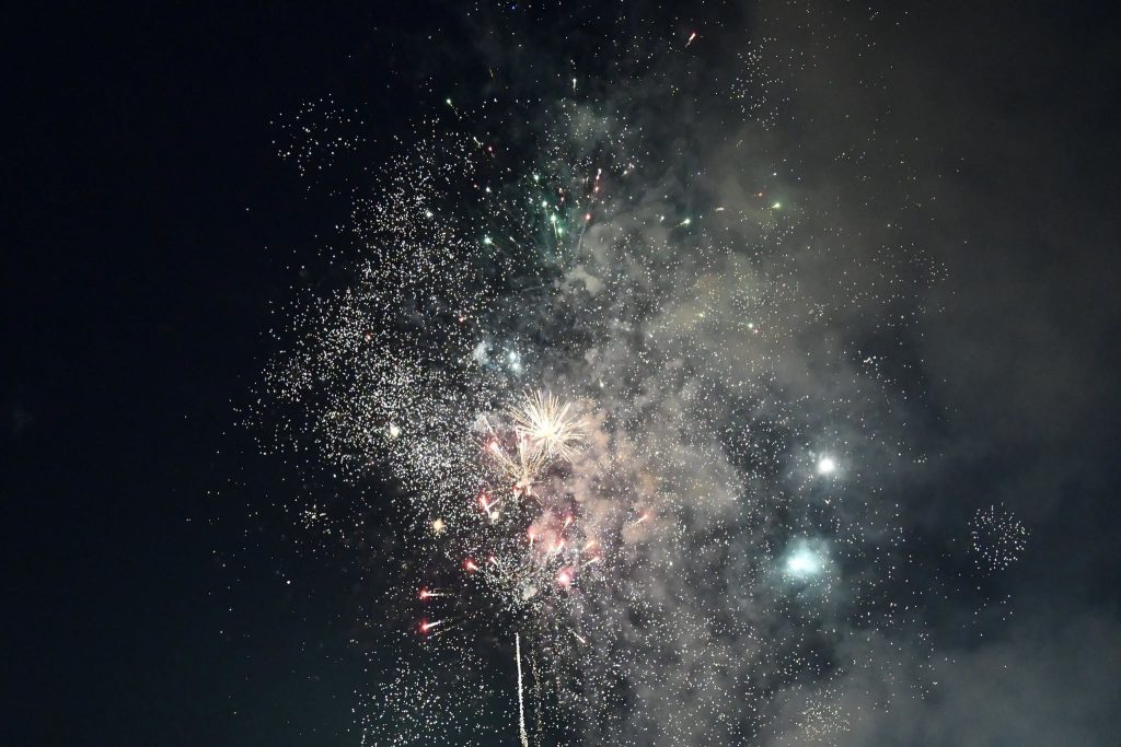 Colorful fireworks exploding in the night sky, surrounded by smoke and sparkling lights.