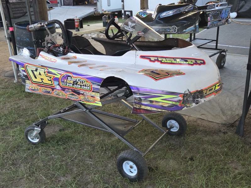A white go-kart with colorful decals and the number 04 sits on a portable stand at an outdoor racing event.