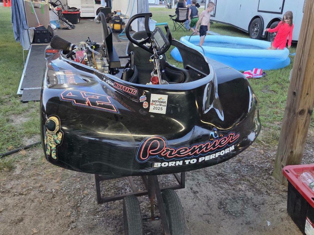 A black go-kart with the text "Premier Born to Perform" and number 42, parked outdoors near children playing in an inflatable pool.