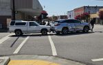 A white pickup truck and a silver SUV involved in a collision at an intersection, with visible damage and people standing nearby on a sunny day.