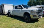 A white Ram pickup truck with a trailer attached, parked on grass under a clear blue sky.