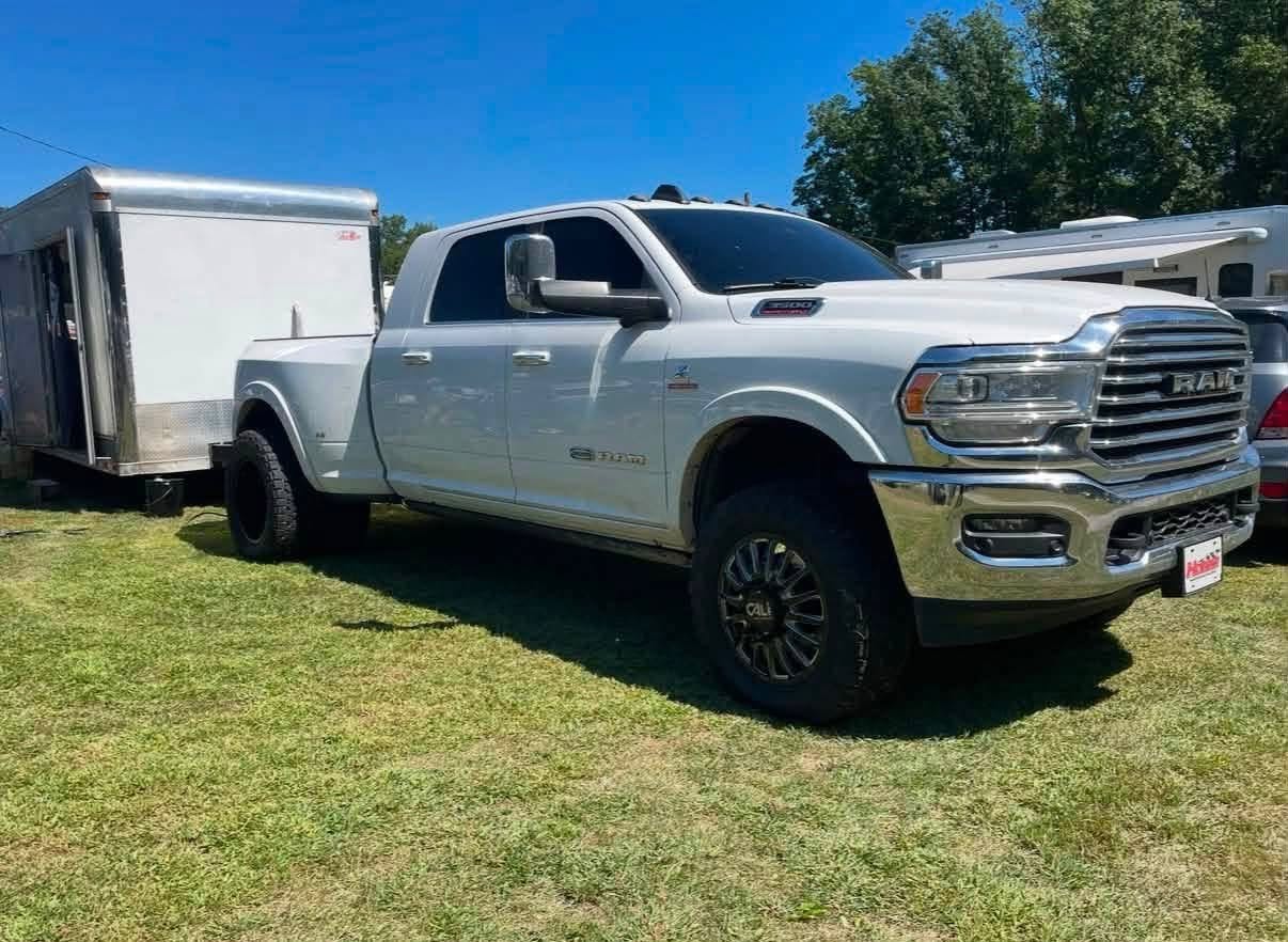 A white Ram pickup truck with a trailer attached, parked on grass under a clear blue sky.