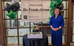 Woman standing beside a table and welcome sign for Dr. Frank-Alston at Northeastern Technical College, surrounded by green, black, and silver star-shaped balloons.