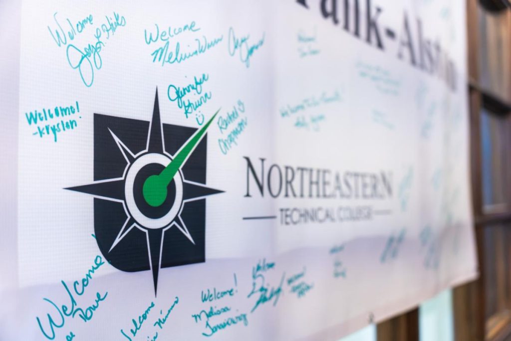 Banner for Northeastern Technical College with a compass logo, covered in handwritten welcome messages and signatures in blue marker.