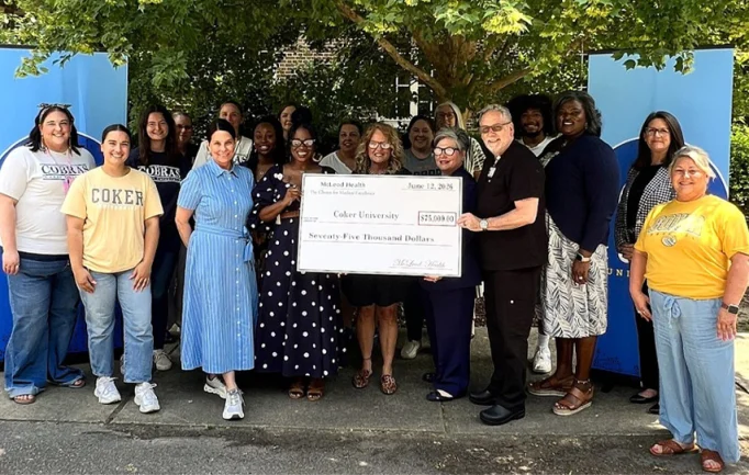 A group of people standing outdoors hold a large ceremonial check for $75,000 made out to Coker University, smiling for the camera.