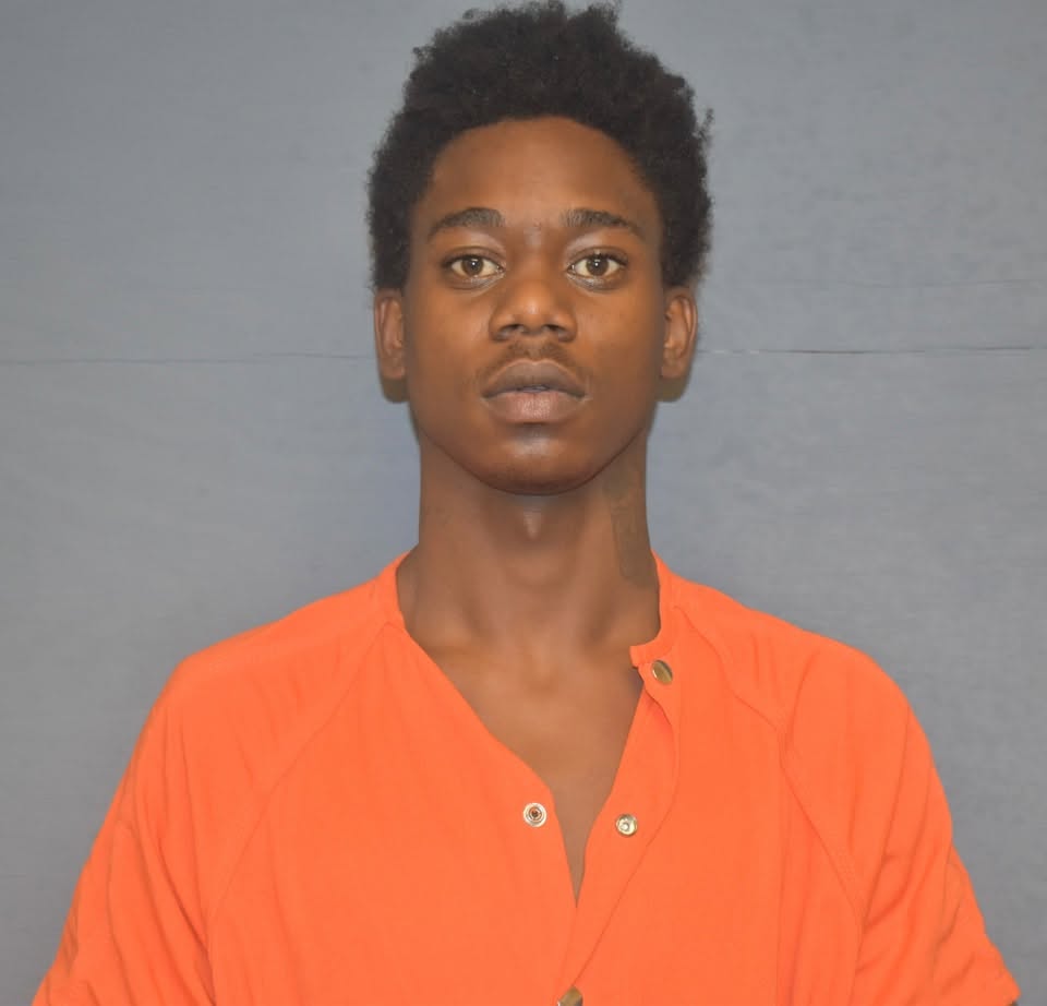 A young man in an orange jumpsuit standing against a plain background, looking directly at the camera.