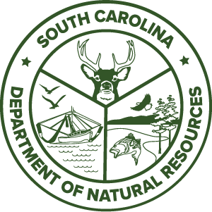 Green circular South Carolina Department of Natural Resources logo featuring a deer head, boat, fish, bird, and trees inside divided sections.